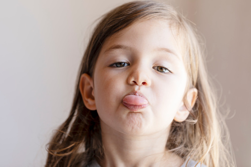 Bored and upset caucasian toddler is showing tongue to camera. She is angry.