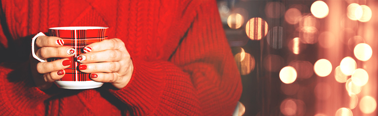 A girl in a red sweater holds a Christmas mug against a background of glowing bokeh. Long banner