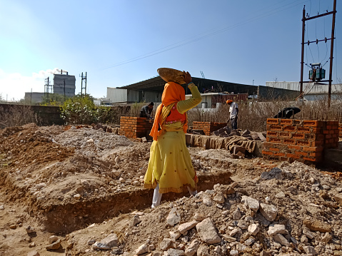 DISTRICT KATNI, INDIA - DECEMBER 13, 2019: An indian lady labour transporting building material on head at construction site.