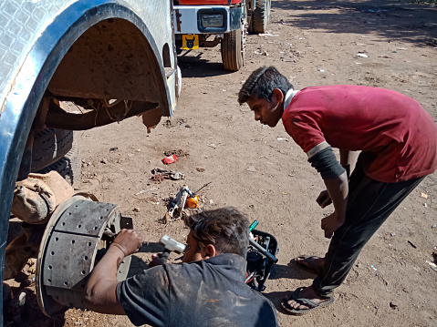 DISTRICT KATNI, INDIA - DECEMBER 14, 2019: Asian Mechanics opening truck wheel screw for repairing task at open automobile workshop field.