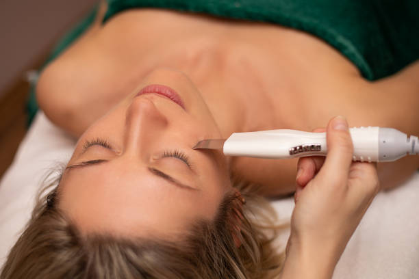 Close-up Of Woman Getting Facial Hydro Microdermabrasion Peeling Treatment At Cosmetic Beauty Spa Clinic. Hydra Vacuum Cleaner. Exfoliation, Rejuvenation And Hydratation. Cosmetology. Face Skin Care. primer plano de la mujer que recibe tratamiento facial de peeling de microdermabrasión en la clínica de spa de belleza cosmética. cuidado de la piel de la cara. limpiador de vacío hydra. exfoliación, rejuvenecimiento e hidratación. cosmetología.