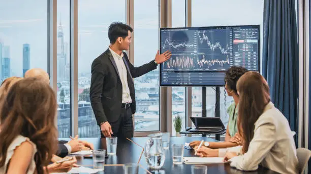 Photo of Successful presentation. Elegant man explaining growth of sales graph, reporting about good result, motivating workers. Multi ethnic team in board room