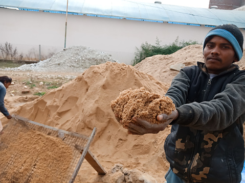 DISTRICT KATNI, INDIA - DECEMBER 18, 2019: An indian village male labour offering sand to camera for photograph at home construction site.