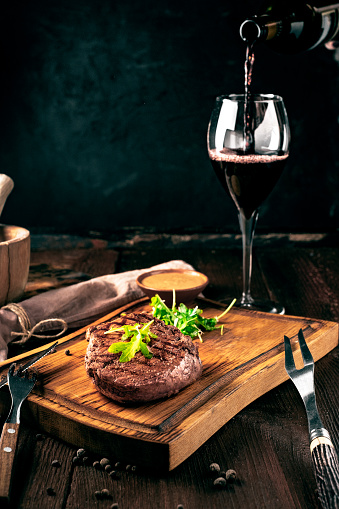 Grilled ribeye beef steak with wine, knife and fork on a wooden Board. Whole roast piece of meat, rustic style