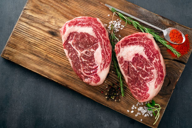 two raw rib eye steak on the butcher's board on a wooden table prepared prepared for cooking. marbled beef top view - dry aged imagens e fotografias de stock