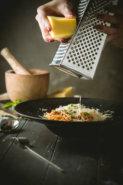 Hands grated Parmesan cheese in spaghetti Bolognese pasta with dried tomatoes and sauce in a black plate on a black wooden background.