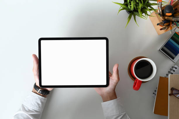 istock Top view of graphic designer hands holding tablet with white screen on white table. 1281227547