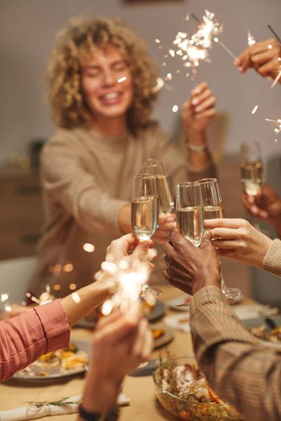 Friends Celebrating Christmas Vertical close up of people toasting with champagne glasses while enjoying dinner party with friends and family and holding sparklers family christmas party stock pictures, royalty-free photos & images