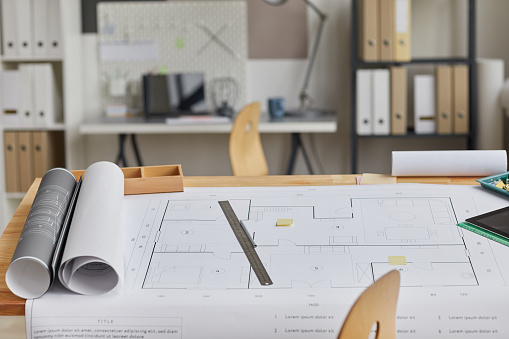 Background image of drawing table with blueprints and tools laid out in forground and architects workplace, copy space