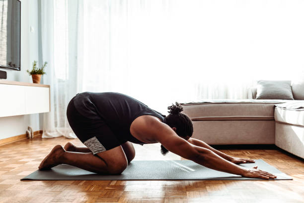 Meditation is hanging out with your soul Shot of a young man going through a yoga routine at home childs pose stock pictures, royalty-free photos & images