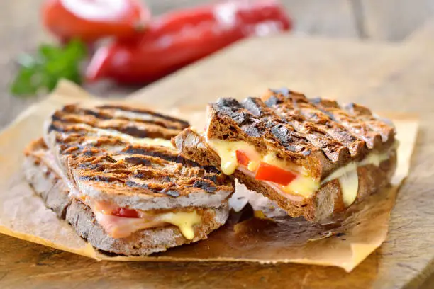 Pressed and toasted rye wholegrain bread with smoked turkey and melted brie cheese served on sandwich paper on a wooden table