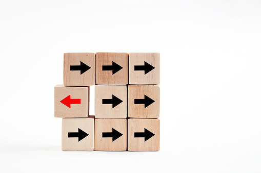 Arrow head icons on wooden blocks with one wooden block pointing to opposite direction. Change in business direction, unique, thinking different or individuality concept.
