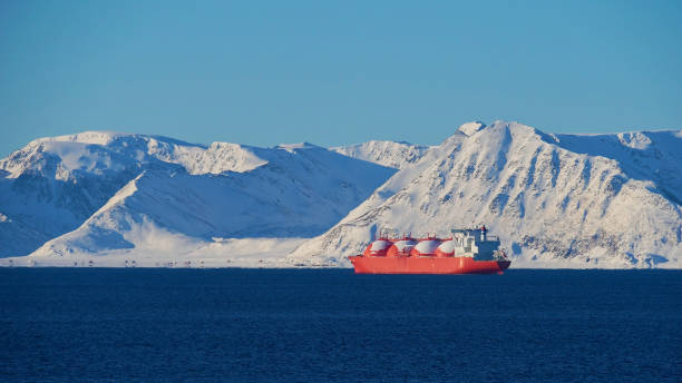 Big red painted LNG (liquefied natural gas) carrier vessel lying at anchor in the arctic ocean in front of Sørøya island with snow-covered mountains near Hammerfest, Norway in winter. stock photo