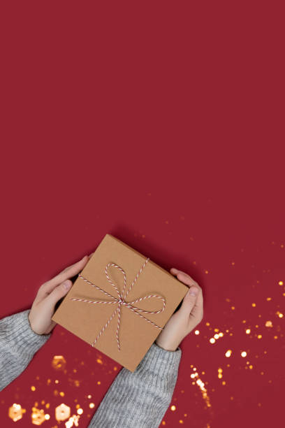 istock Hands hold gift box tied with rope on a red background. 1281247444