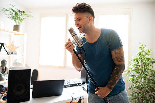 Young, Caucasian, male singer singing his new song into the microphone in the home music recording studio.