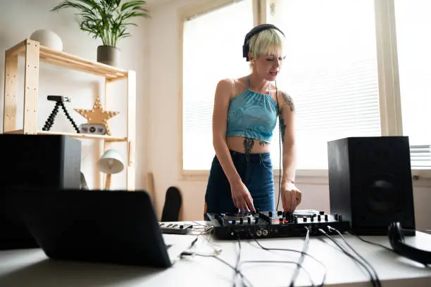 Young, tattooed, Caucasian, female dj and producer practicing mixing music at home.