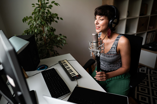 Young, Caucasian, female singer enjoying singing and recording eyes closed for her new song, surrounded with audio equipment in the home music recording studio.