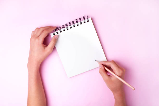 istock Two hands hold a notepad on a pink background. To do list. View from above 1281250134