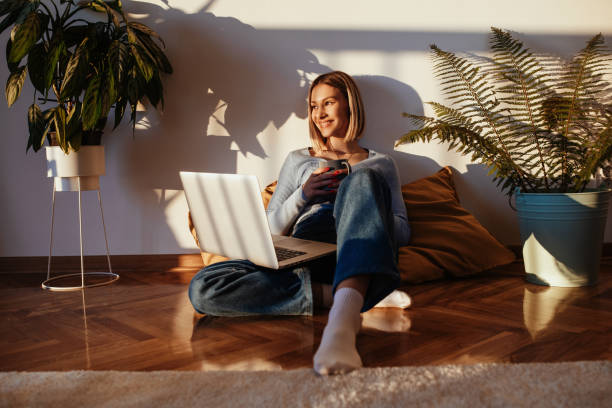 Young woman working on laptop at home, thinking and smiling