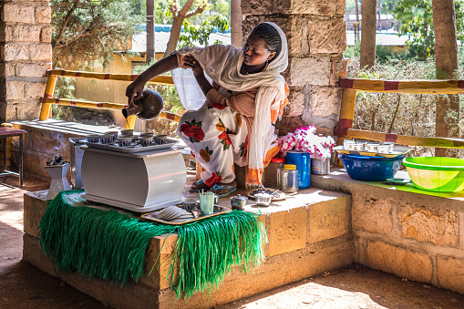 Yeha, Ethiopia - Feb 10, 2020: Young woman in traditional clothing is preparing a coffee ceremony at the Great Temple of the Moon. This ceremony is an important part of the Ethiopian culture.