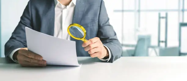 Photo of businessman or tax inspector analyzing document with magnifying glass in office. business financial audit concept. copy space