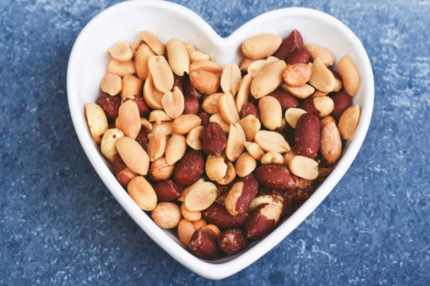 istock Peanuts in a heartshaped bowl on a blue background 1281255994