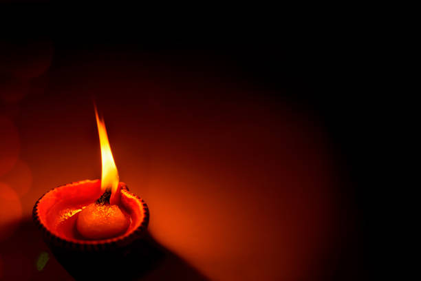 Happy Diwali - One Diya oil clay lamp illuminated during Diwali celebration with copy space. Hindu culture ritual festive celebration during corona pandemic at home.