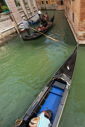 Venice, Veneto, Italy - Sept 13th, 2015: Two gondoliers and tourists on the gondolas, typical Venetian rowing boat. Sightseeing tour along the Canals of the famous city. Veneto, Italy, Europe. The gondola is a traditional, flat-bottomed Venetian rowing boat, well suited to the conditions of the Venetian lagoon. It is similar to a canoe, except it is narrower. It is propelled by a gondolier, who uses a rowing oar, which is not fastened to the hull, in a sculling manner and acts as the rudder.