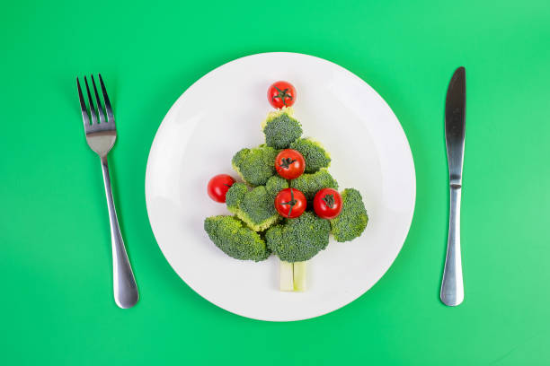 istock Christmas tree of organic vegetables on white plate; Broccolis and tomatoes with fork and knife on green background. Merry Xmas and happy New Year party, New You, Healthy food and vegetarian concept 1281258845