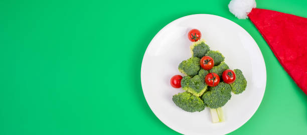 istock Christmas tree of organic vegetables on white plate; Broccolis and tomatoes with fork and knife on green background. Merry Xmas and happy New Year party, New You, Healthy food and vegetarian concept 1281259708