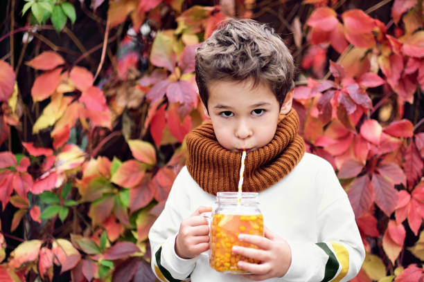 cute fashionable boy holding a sea buckthorn drink on a background of wild grapes stock photo