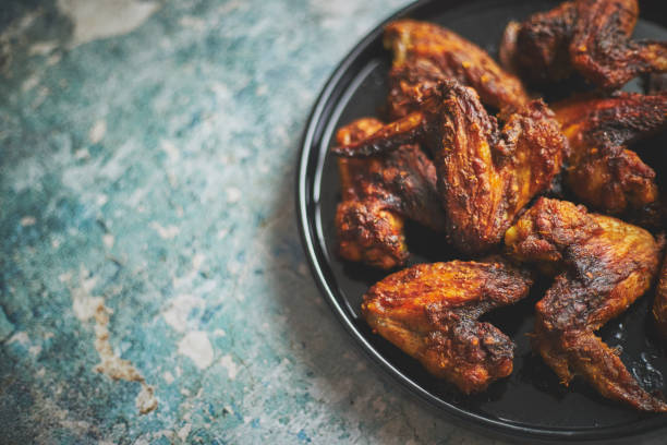 istock Grilled chicken wings on a black ceramic plate. Placed on a stone 1281260332