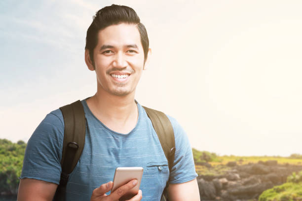 istock Asian man with a backpack holding smartphone with a lake view and blue sky background 1281263497
