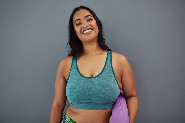 Feels good to get fit Portrait of a confident young woman holding an exercise mat against a grey studio background sports bra stock pictures, royalty-free photos & images