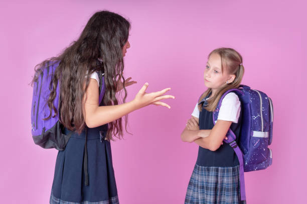 two schoolgirls are quarreling on a pink background. one girl does not react to another girl's aggression. concept of the day international day of non violence. - mockery imagens e fotografias de stock