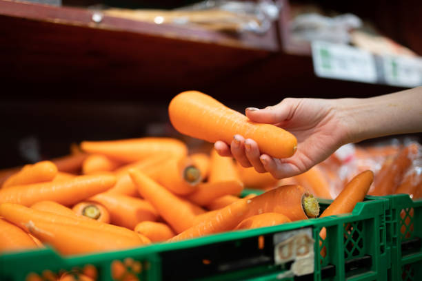 istock Women's hands picking up carrots in a supermarket 1281269354