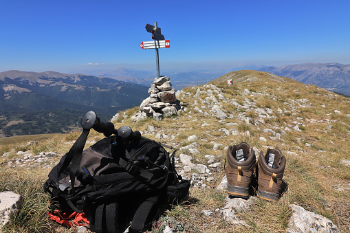 On the ground backpack, trekking poles and boots taken off: rest on the summit of Monte Rotella (2129 m a.s.l.) after having covered the long ridge of about 7 km. In the background the signs indicating the paths that lead downstream. On the horizon, Monte Genzana on the left, Monte Morrone on the right. Territory of Pescocostanzo, Majella National Park, Abruzzo, Italy.