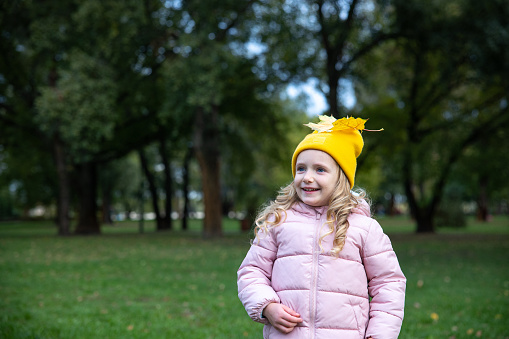 Portrait of a happy little girl. A yellow maple leaf lies on the girl's hat.
