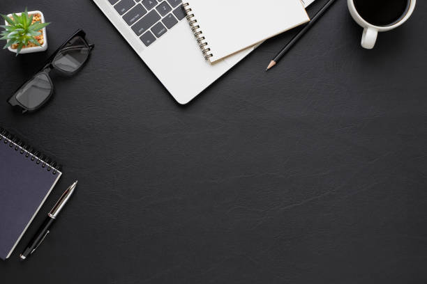 istock Top view above of Black leather office desk table with keyboard, notebook and coffee cup with equipment other office supplies. Business and finance concept. Workplace, Flat lay with blank copy space. 1281275219