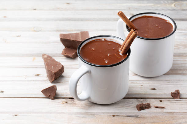 istock Two mugs hot chocolate with cinnamon, nuts on wood background decorated with chocolate pieces 1281276596