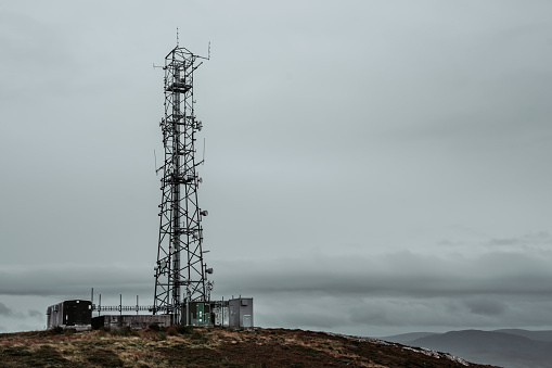 A tele radio tower on top of a mountain near a haystack