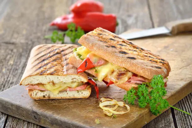 Grilled Italian ciabatta bread with ham, cheese and vegetables served on a wooden cutting board