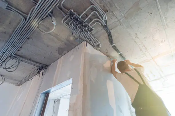 Worker is installing the electrical wires on the ceiling that is the part of internal wiring in apartment is under construction, remodeling, renovation, extension, restoration and reconstruction. Concept of clever house