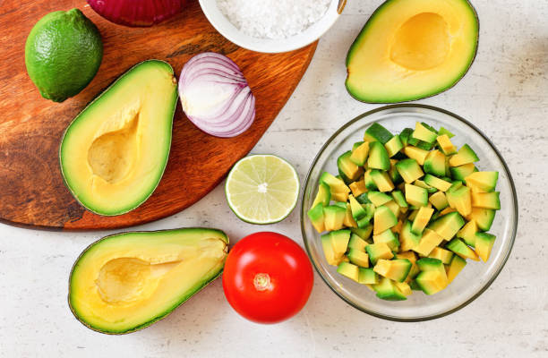 istock Avocado halves, some cut to small pieces, limes, tomato and onion - basic guacamole ingredients on white working board, view from above 1281283290