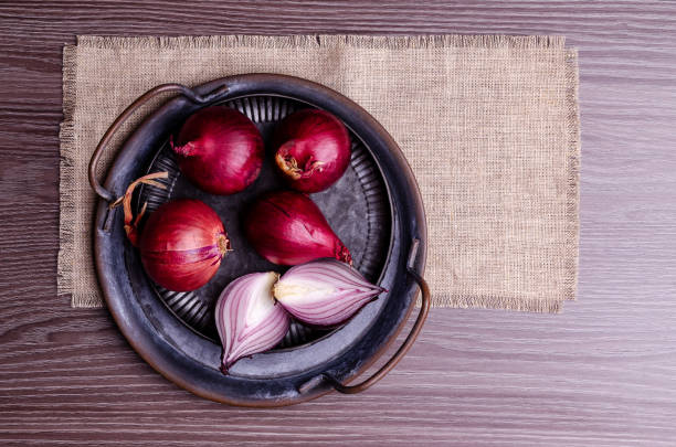 Raw red onion in a metal plate on a dark wooden background. Selective focus.