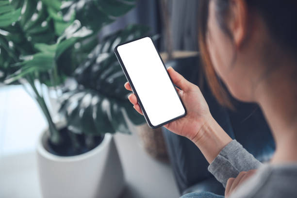 istock Smartphone mockup. Women hand using mobile phone on sofa at home office. White screen empty space for design concept. 1281290541