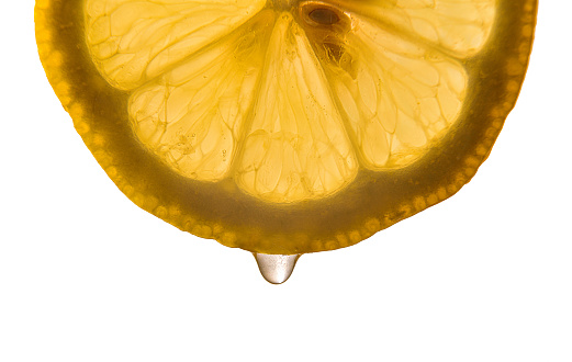 Detail of half lemon slice backlit with juice falling white isolated background. Horizontal composition.