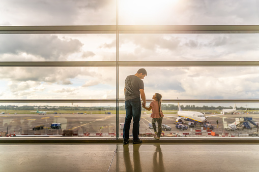 Silhouette of family, father and daughter on airport terminal. Holding hands and looking at each other, waiting for departure. Dublin, Ireland
