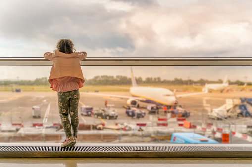 Silhouette of young girl on airport terminal. Standing on windowsill and looking on airplanes, waiting for departure. Dublin, Ireland