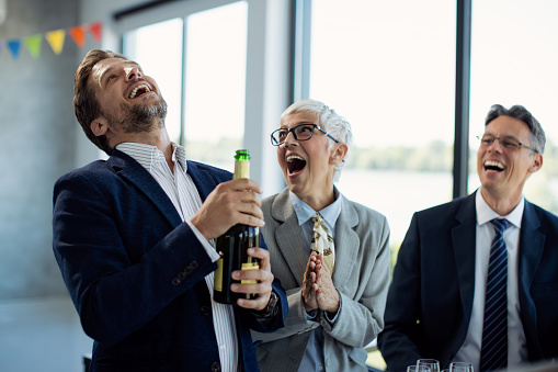 Happy coworkers having fun while opening bottle of Champagne and  celebrating their business achievement on a party in the office.